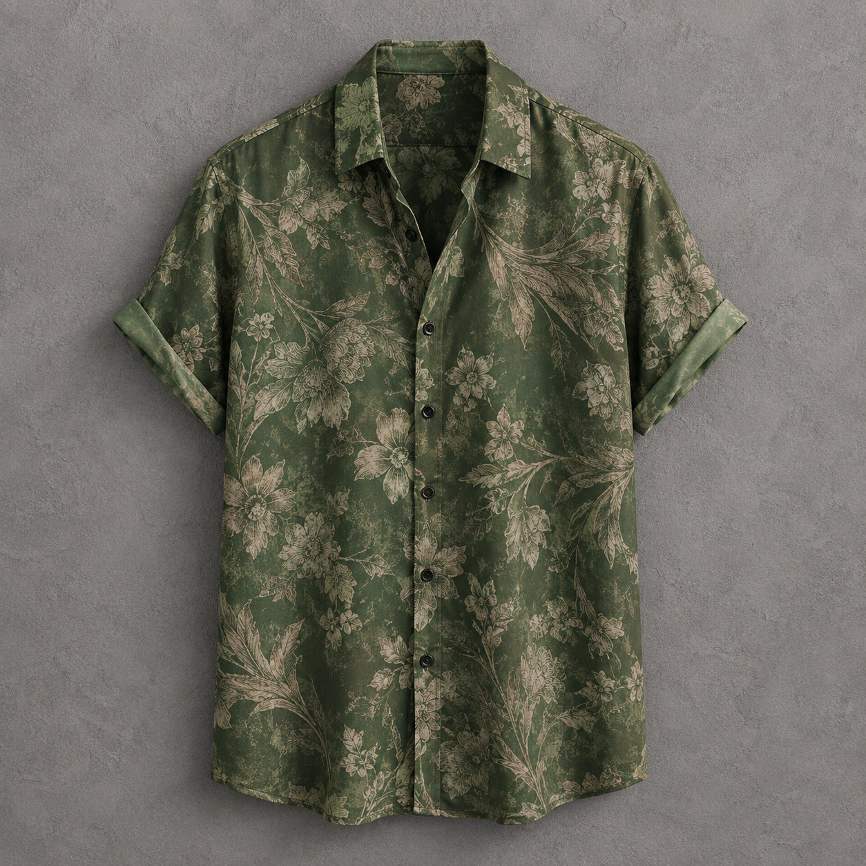 A short-sleeve button-up shirt in olive green with a beige floral pattern, laid flat against a textured gray background.