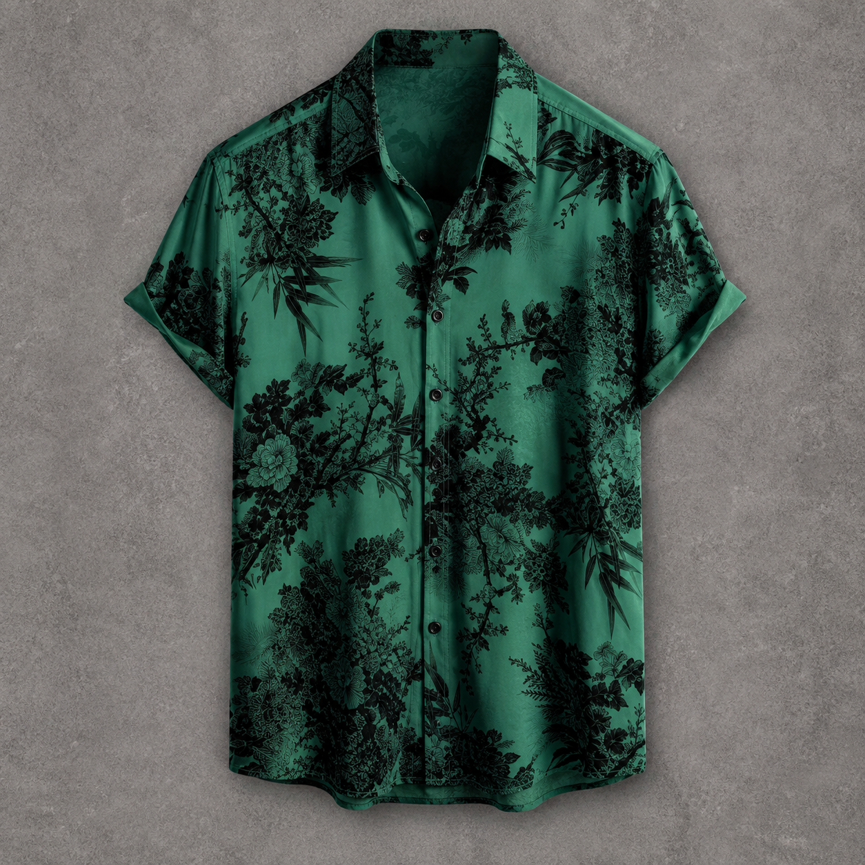 A short-sleeve button-up shirt in emerald green with a black floral and botanical print, displayed flat against a textured gray background.