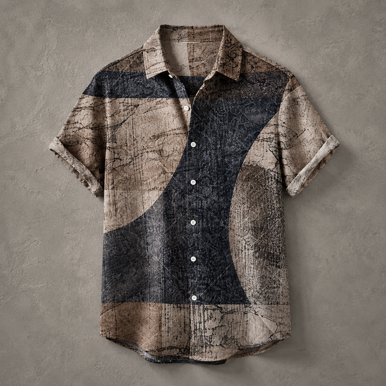 A short-sleeve button-up shirt with a distressed abstract geometric pattern in beige, brown, and charcoal gray, laid flat against a textured gray background.
