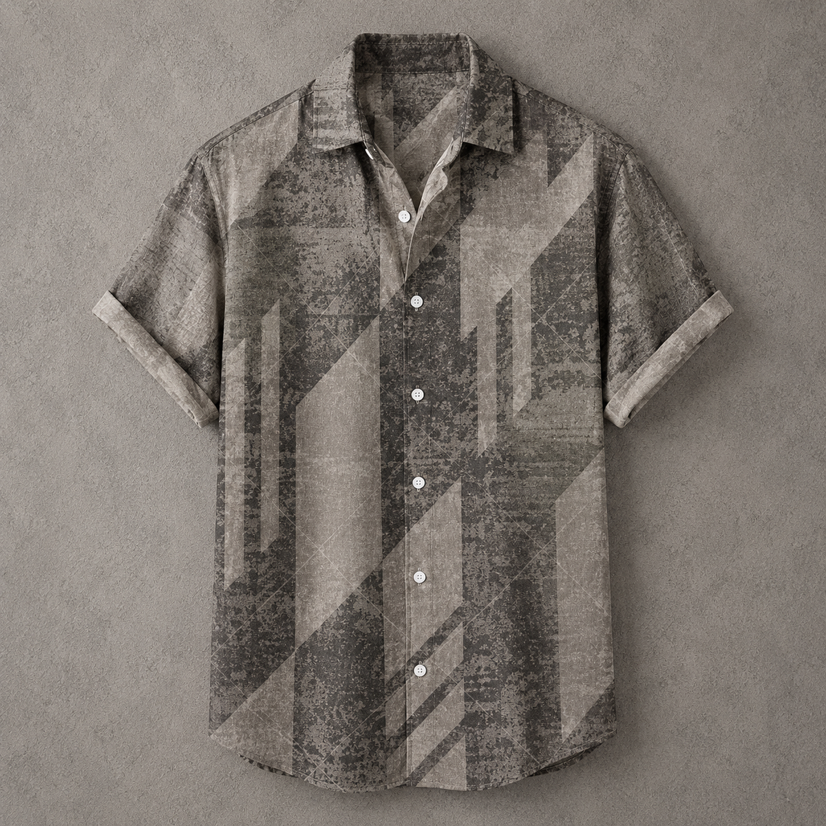 A short-sleeve button-up shirt with a distressed geometric pattern in shades of gray, brown, and beige, laid flat on a textured gray background.