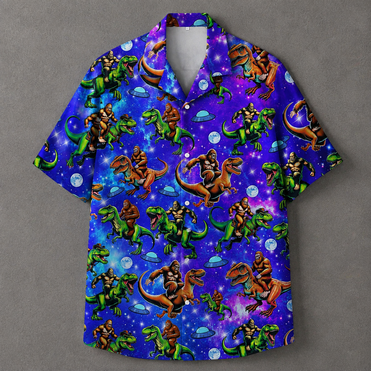 A short-sleeve button-up camp shirt with a vibrant purple and blue space print featuring cartoon gorillas riding green and brown dinosaurs, set against a solid gray background.