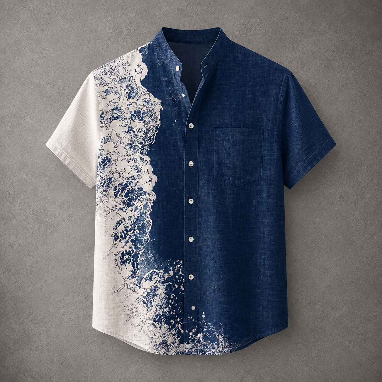 A men's short-sleeve button-up shirt with a split design: one side is solid navy blue, and the other side features a large white wave pattern over a light base. The shirt has a mandarin collar, a left chest pocket, and white buttons, shown against a textured gray background.