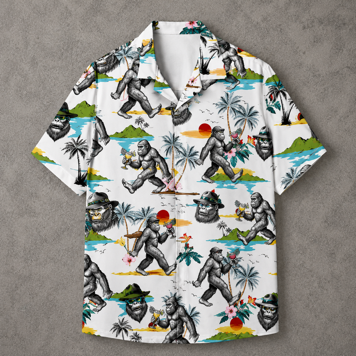 A short-sleeve button-up camp shirt with a white base and a detailed graphic print of gorillas in tropical beach scenes, laid flat on a textured gray background.