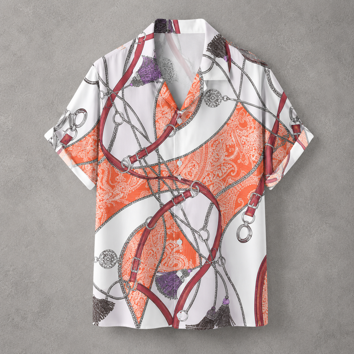A short-sleeve button-up camp shirt with an equestrian-inspired print featuring orange and white paisley, red leather straps, silver chains, and purple tassels, displayed flat against a textured gray background.