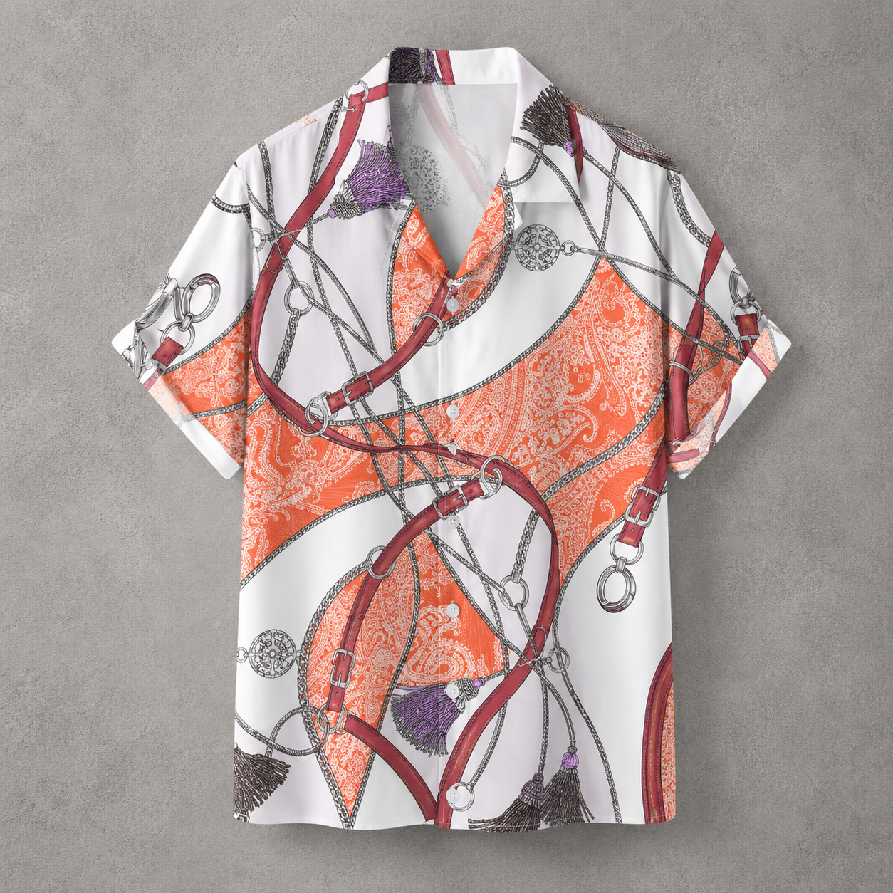 A short-sleeve button-up camp shirt with an equestrian-inspired print featuring orange and white paisley, red leather straps, silver chains, and purple tassels, displayed flat against a textured gray background.