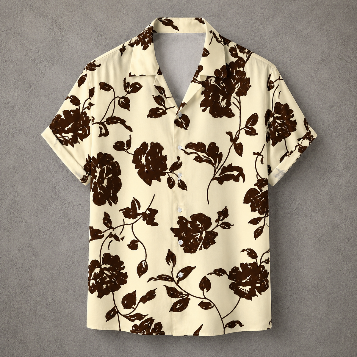 A short-sleeve camp collar button-up shirt with a dark brown floral print on a cream background, displayed flat against a textured gray backdrop.