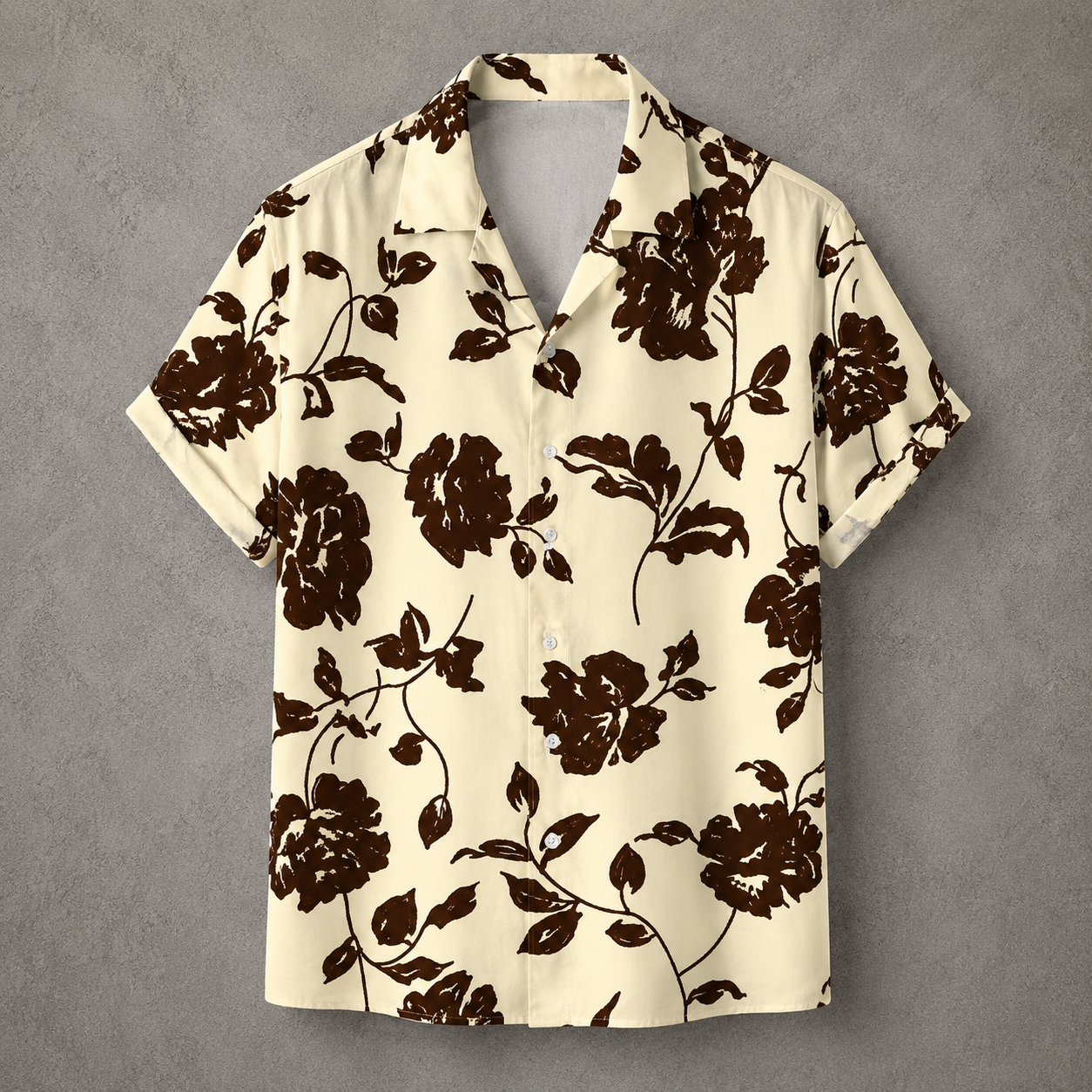 A short-sleeve camp collar button-up shirt with a dark brown floral print on a cream background, displayed flat against a textured gray backdrop.