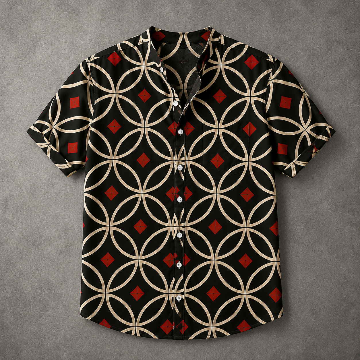 A short-sleeve button-up shirt with a black base and a geometric pattern of interlocking beige circles and red diamonds, laid flat on a textured gray background.