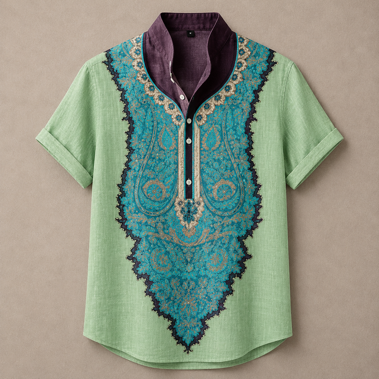 A short-sleeve button-front shirt laid flat on a neutral beige background. The shirt has a light mint green base with a large turquoise and gold paisley-style yoke panel, a dark purple inner placket and collar, and a dark purple scalloped border outlining the front design.