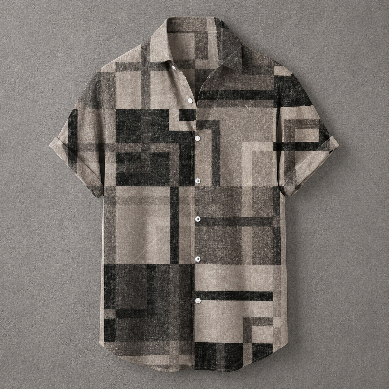A short-sleeve button-up shirt with a geometric block pattern in beige, gray, and black, displayed flat against a textured gray background.