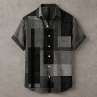 A short-sleeve button-up shirt with a geometric block pattern in black, gray, and charcoal, laid flat against a textured gray background.