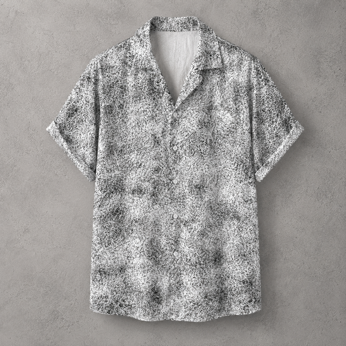 A short-sleeve button-up shirt with a black and white abstract textured pattern, displayed flat against a gray concrete-textured background.