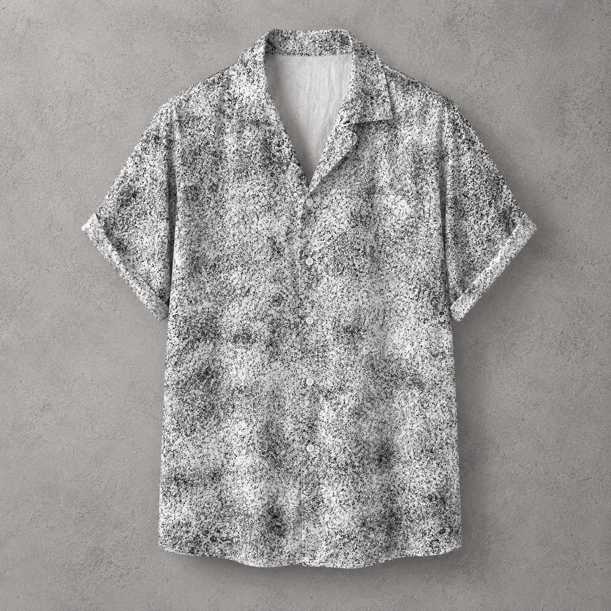 A short-sleeve button-up shirt with a black and white abstract textured pattern, displayed flat against a gray concrete-textured background.