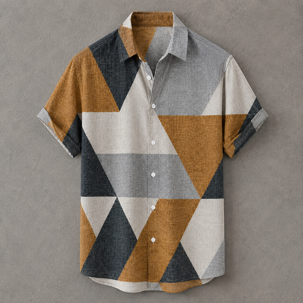 A short-sleeve button-up shirt with a geometric triangle pattern in mustard yellow, gray, off-white, and dark charcoal, displayed flat against a textured gray background.