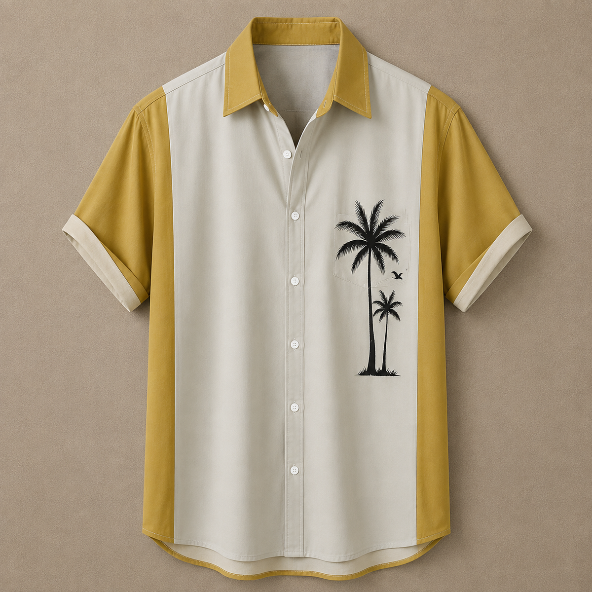 A short-sleeve button-up shirt with a colorblock design of mustard yellow and cream, featuring a black palm tree graphic on the chest, displayed against a neutral textured background.