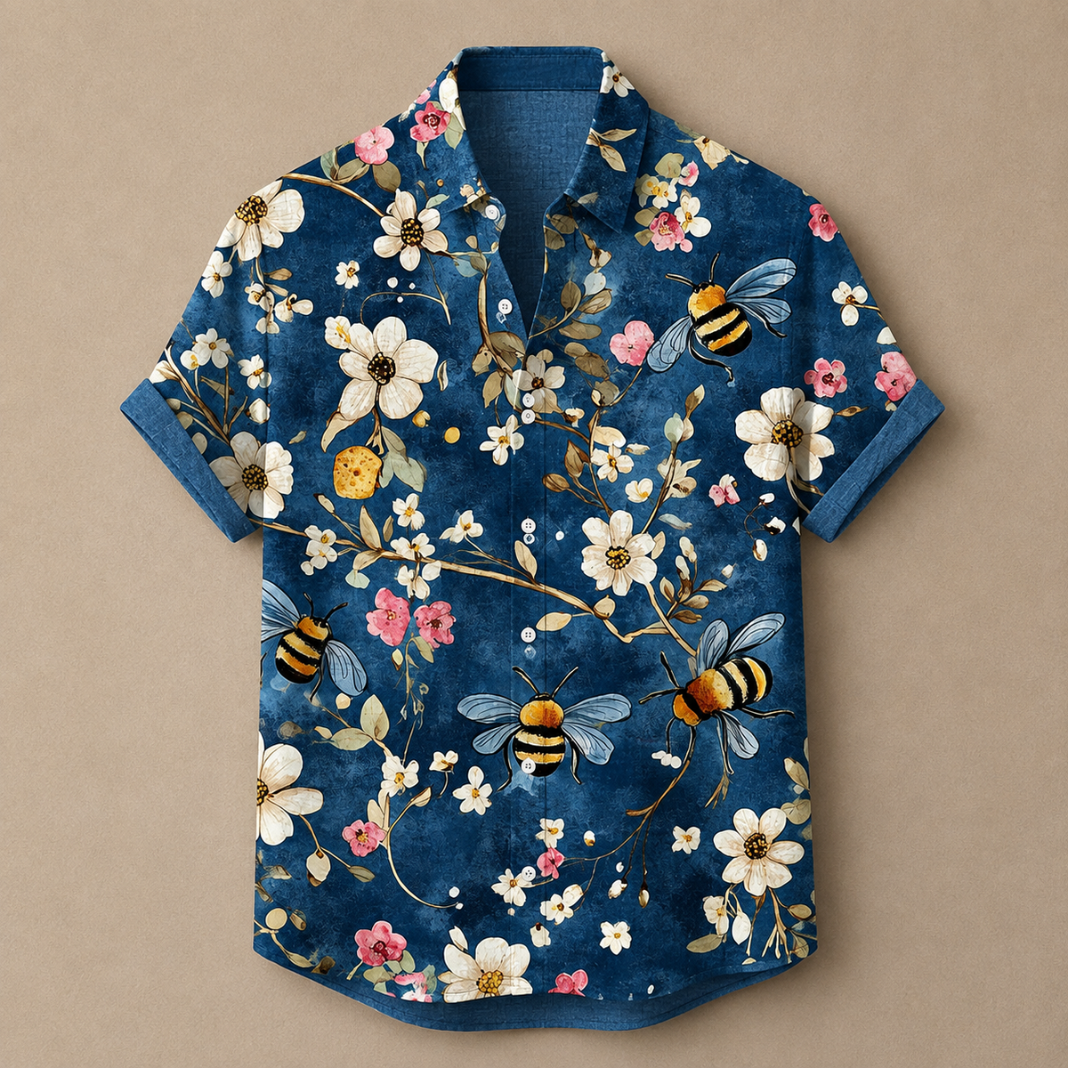 A short-sleeve button-up shirt with a dark blue base, featuring a detailed print of white flowers, pink blossoms, yellow and black bumblebees, and small green leaves, laid flat against a solid beige background.