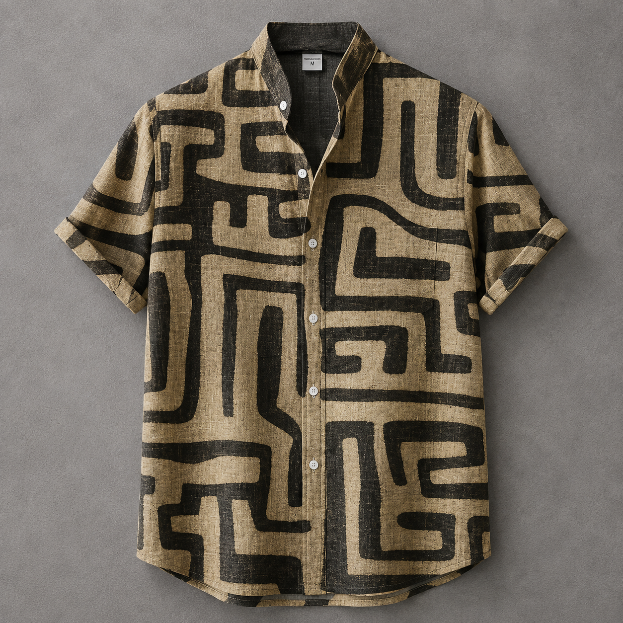 A short-sleeve button-up shirt with a beige and black maze-like geometric pattern, laid flat on a textured gray background.