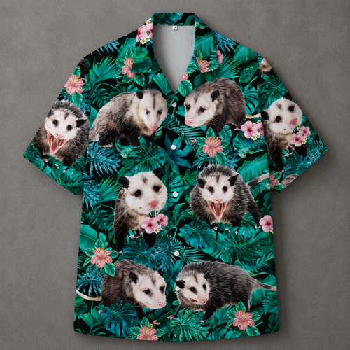 A short-sleeve button-up camp shirt featuring a tropical print of green palm leaves and pink flowers, overlaid with repeated images of opossums, displayed flat against a gray background.