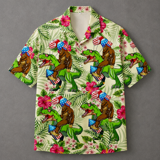 A short-sleeve camp collar button-up shirt with a vibrant, all-over graphic print. The pattern features green dinosaurs riding brown gorillas, decorated with American flags, set against a tropical background of palm leaves, pink hibiscus flowers, and blue-and-white flags, all on a light cream base.