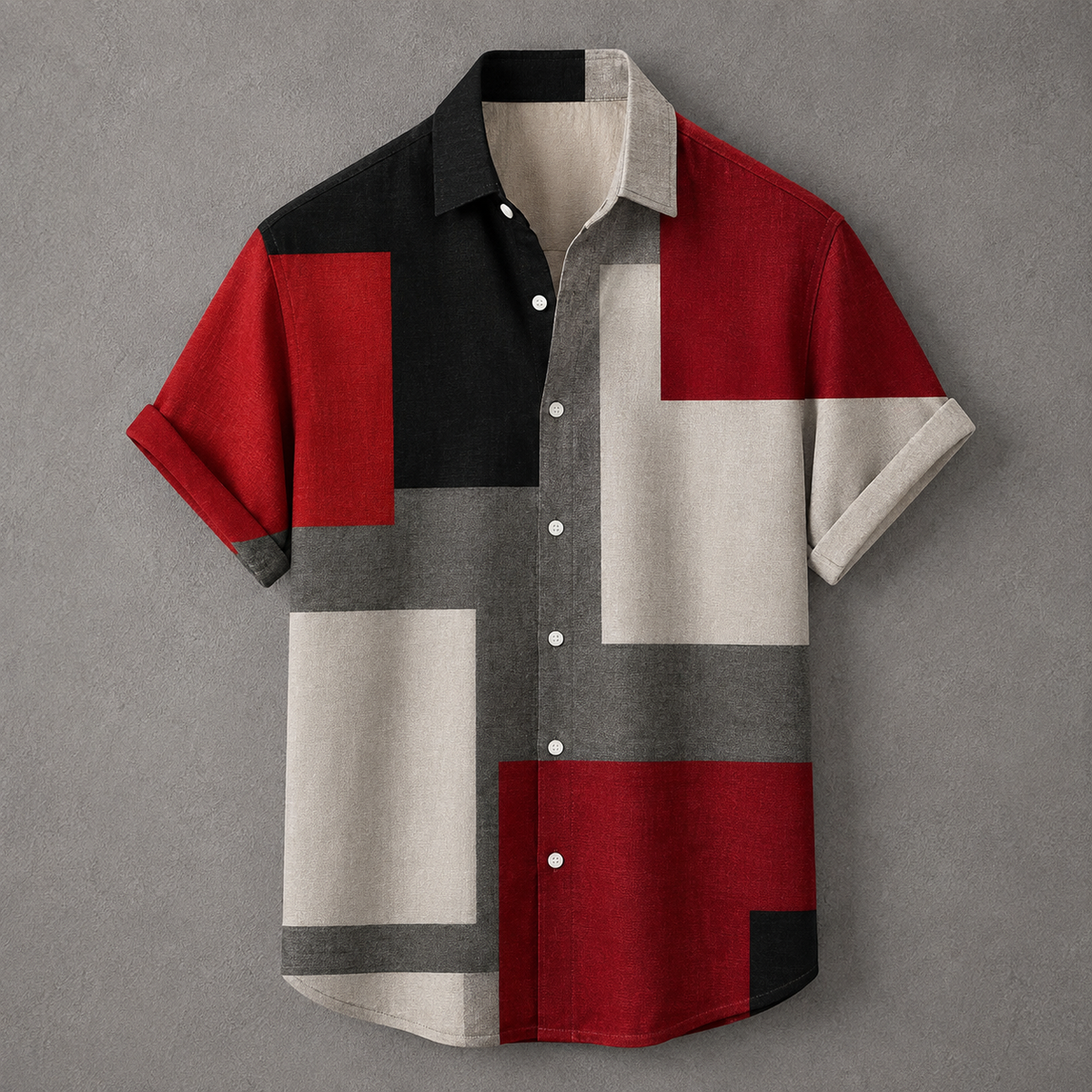 A short-sleeve button-up shirt with a geometric color-block pattern in red, black, gray, and off-white, displayed flat against a textured gray background.