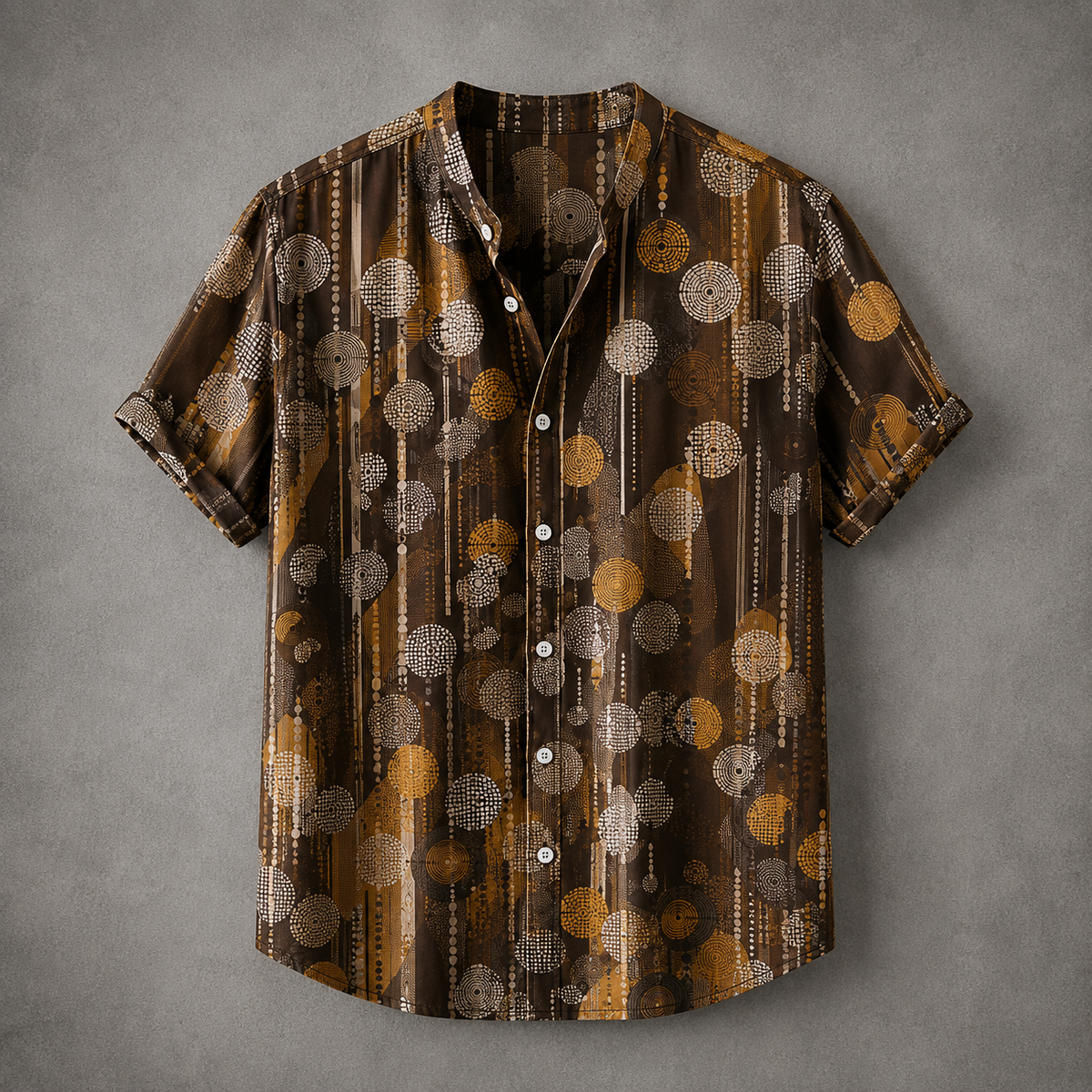 A short-sleeve button-up shirt with a brown, gold, and beige abstract pattern of circles and vertical stripes, laid flat on a textured gray background.