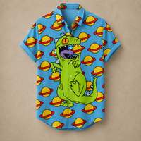 A short-sleeve button-up shirt in bright blue, featuring a cartoon green dinosaur with a gold crown and a repeating pattern of yellow planets with red rings, laid flat on a beige background.