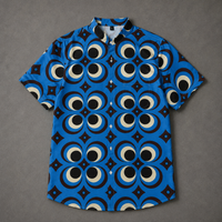 A short-sleeve button-up shirt with a vibrant blue base and a bold geometric pattern of large circular eyes and black diamond shapes, laid flat on a textured gray background.