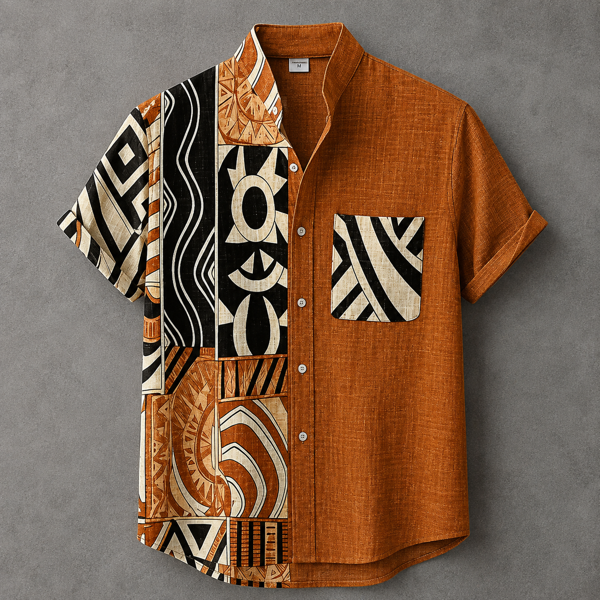 A short-sleeve button-up shirt laid flat on a textured gray background. The shirt features a solid rust-orange body with a split design: one half is solid rust-orange, while the other half displays a patchwork of black, rust-orange, and cream geometric and tribal patterns.