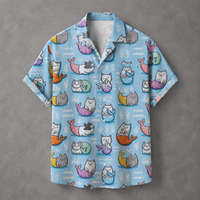 A light blue short-sleeve button-up shirt with an all-over print of cartoon mermaids in pastel colors, laid flat on a textured gray background.