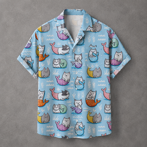 A light blue short-sleeve button-up shirt with an all-over print of cartoon mermaids in pastel colors, laid flat on a textured gray background.