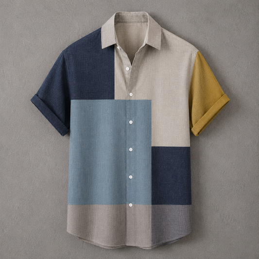 A short-sleeve button-up shirt with a geometric color-block pattern in navy blue, light blue, beige, gray, and mustard yellow, displayed flat against a textured gray background.