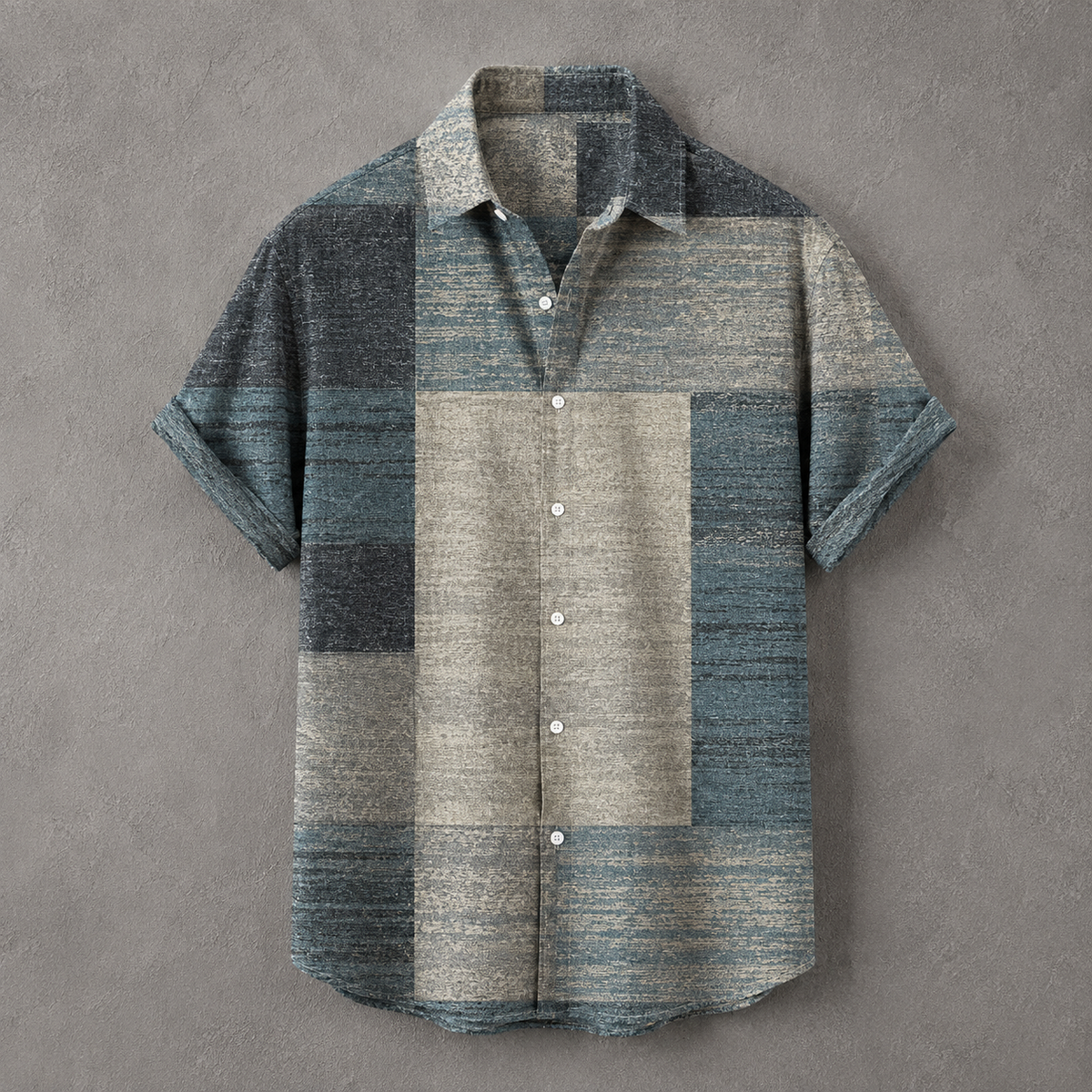 A short-sleeve button-up shirt with a textured patchwork design in muted blue, gray, and beige tones, laid flat against a textured gray background.
