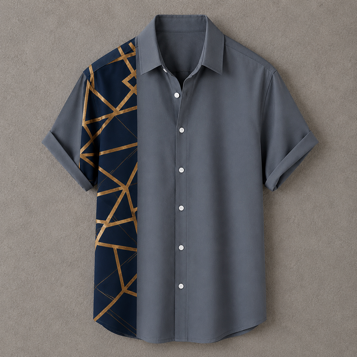 A short-sleeve button-up shirt laid flat on a textured gray background. The shirt is primarily slate gray with a contrasting dark navy panel on the wearer's left side featuring a geometric gold line pattern.