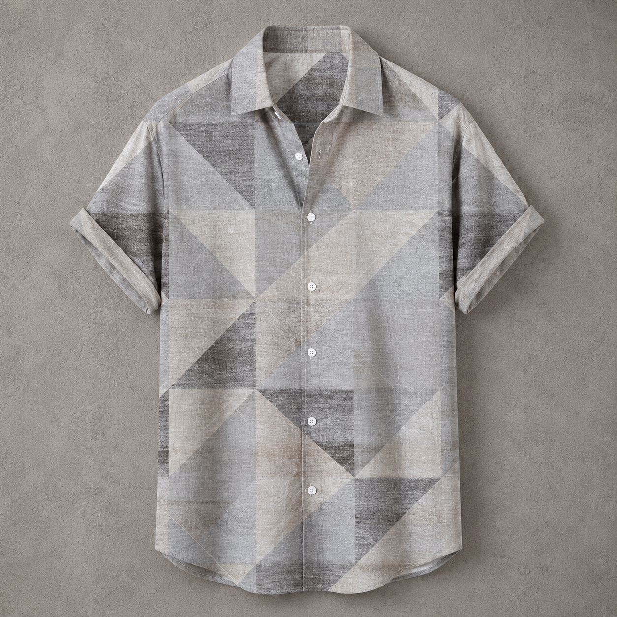 A short-sleeve button-up shirt with a geometric triangle pattern in shades of gray, beige, and taupe, laid flat against a textured gray background.