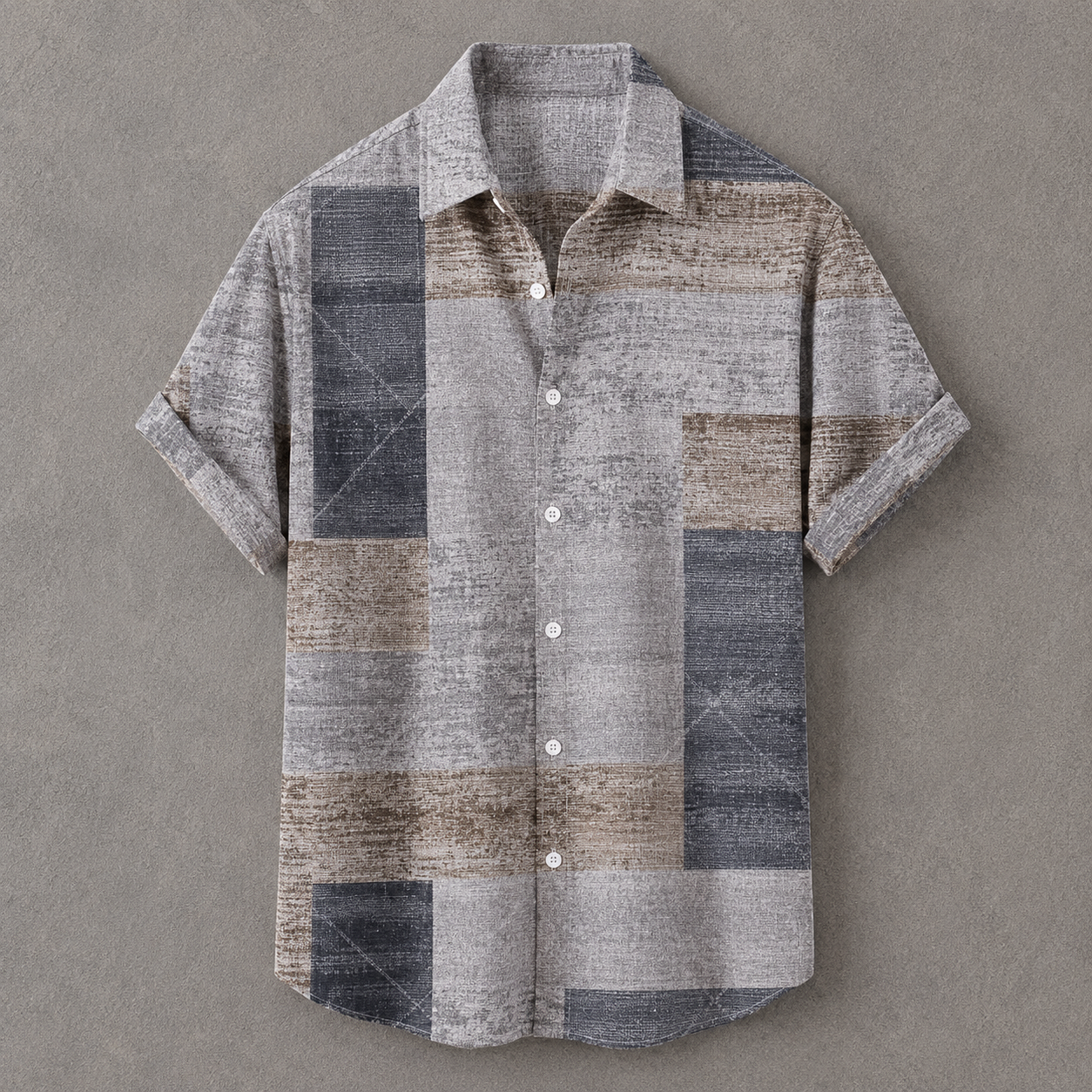 A short-sleeve button-up shirt with a textured patchwork design in shades of gray, beige, and blue, laid flat on a neutral gray background.