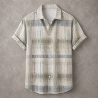 A short-sleeve button-up shirt with a textured, abstract plaid pattern in muted beige, gray, and soft blue tones, laid flat against a textured gray background.